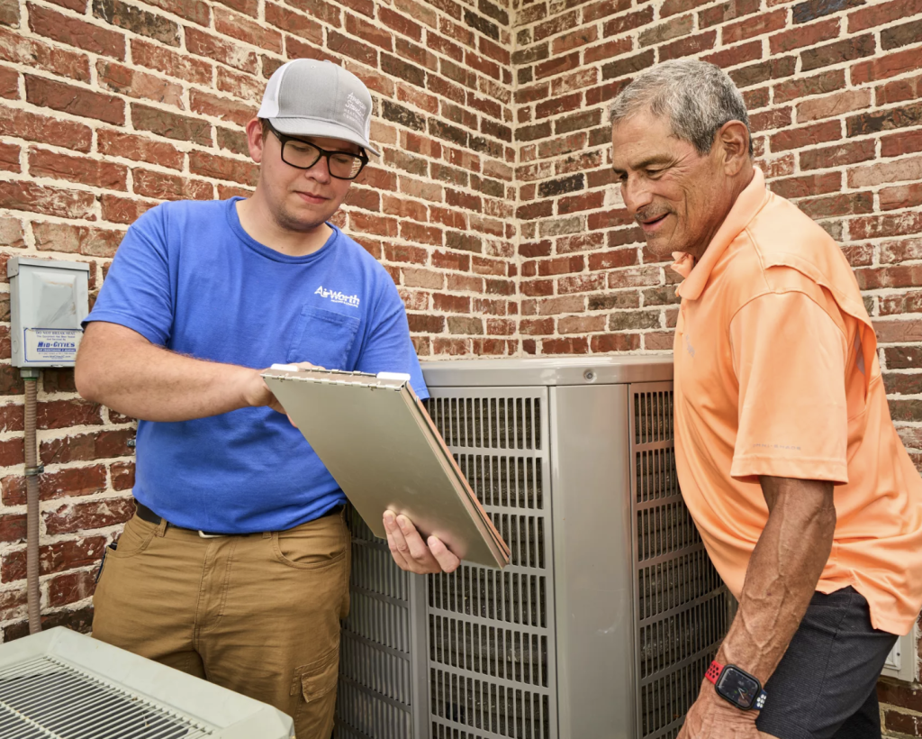 Technician from Air Worth Heating & Cooling reviewing HVAC system details with a client near outdoor air conditioning unit, emphasizing commercial HVAC installation and maintenance services.